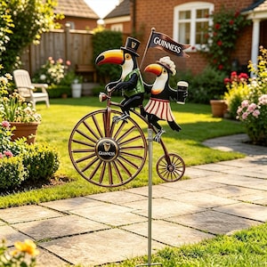 Puede incluir: Un adorno de jardín caprichoso con dos tucanes montados en un biciclo. La bicicleta es marrón con una rueda delantera grande y el logotipo de Guinness. Un tucán lleva un sombrero de copa y el otro sostiene una pinta de Guinness. Una bandera de Guinness ondea.