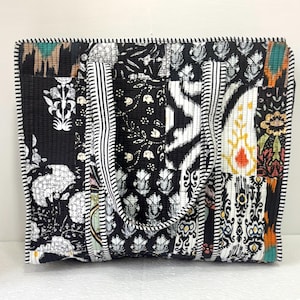 May include: A patchwork tote bag with a variety of black and white patterns. The bag features floral, geometric, and striped designs. The edges are trimmed with a black and white striped border. The bag has two handles with a striped design.