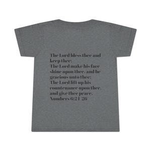 Op de afbeelding: Een grijs t-shirt met de tekst "The Lord bless thee and keep thee: The Lord make his face shine upon thee, and be gracious unto thee: The Lord lift up his countenance upon thee, and give thee peace. Numbers 6:21 26."