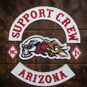 May include: A set of embroidered patches featuring a white arched top rocker with red text reading SUPPORT CREW, a white bottom rocker with red text reading ARIZONA, two small diamond patches with red text MC and 1%, and a central skull with flames.