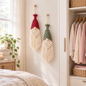 May include: Two macrame wall hangings shaped like gnomes, one with a red hat and one with a green hat. Both feature a natural cream-colored cord beard, a round wooden bead for a nose, and a braided cord loop at the top for hanging on a wall.