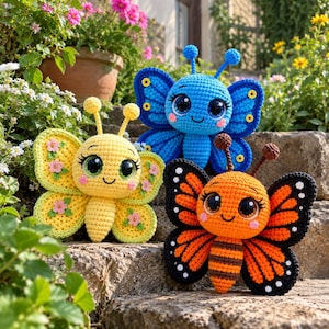 May include: Three crocheted butterfly plush toys featuring large black eyes and antennae. One is yellow with pink flower accents, one is blue with yellow circular details on the wings, and one is orange and black with a striped body and white spots.