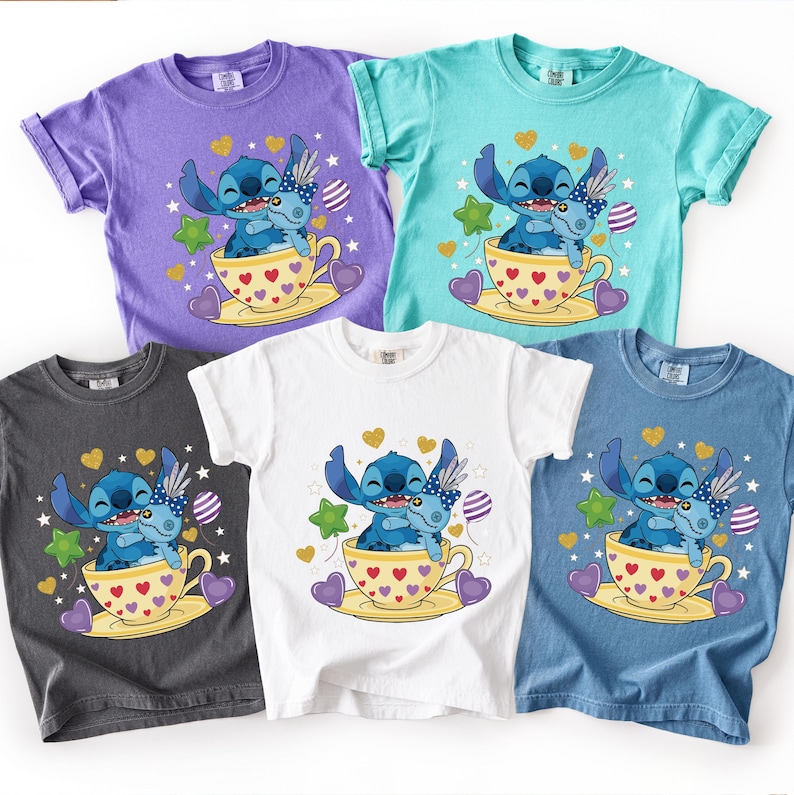 May include: Five short-sleeved t-shirts in purple, teal, white, charcoal grey, and blue. Each shirt features a cartoon illustration of a blue alien character in a teacup, surrounded by hearts and stars.