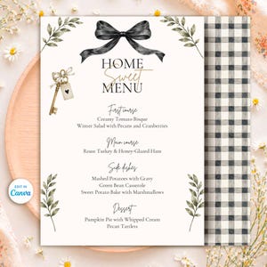 Op de afbeelding: Een menukaart met de titel HOME SWEET MENU, voorzien van een zwarte strik, een gouden sleutel met een hartvormig label en groene bladeren. De tekst bevat gerechten zoals tomatensoep en kalkoen. Afgewerkt met een zwart-witte ruitrand.