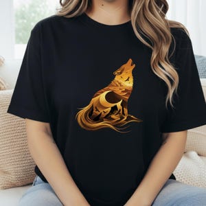A woman wearing a black t-shirt featuring a detailed golden wolf silhouette. Inside the wolf is a desert landscape with sandstone buttes, a crescent moon, and vultures flying over sand dunes.