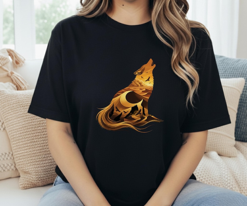 A woman wearing a black t-shirt featuring a detailed golden wolf silhouette. Inside the wolf is a desert landscape with sandstone buttes, a crescent moon, and vultures flying over sand dunes.