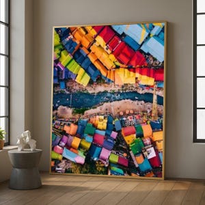 Può includere: Una stampa artistica incorniciata con una vista aerea di una città vivace. L'opera d'arte presenta una colorata serie di edifici con tetti dipinti in tonalità di rosso, arancione, giallo, verde e blu. Un fiume attraversa la scena.