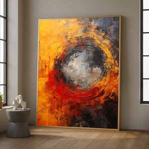 Pode incluir: Grande pintura abstrata com moldura dourada. A obra apresenta um design circular com um centro escuro, rodeado por camadas de pinceladas laranja, vermelha e preta. A pintura é exibida numa sala com luz natural.