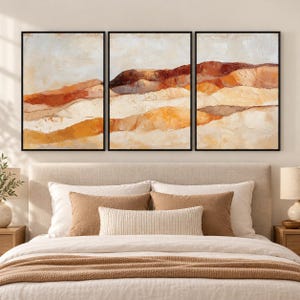 May include: A triptych wall art set featuring three framed rectangular canvases displaying an abstract landscape painting with layered horizontal bands of cream, beige, ochre, and deep burnt orange tones with visible textured brushstrokes.