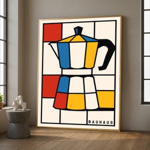 Pode incluir: Uma impressão artística emoldurada com um design geométrico colorido de uma cafeteira. A obra de arte usa cores primárias e linhas pretas, com a palavra "BAUHAUS" na parte inferior. A impressão está em uma moldura dourada.