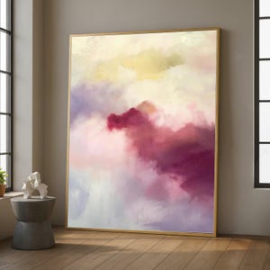 Può includere: Stampa artistica astratta con cornice dorata. L'opera presenta una miscela di colori, tra cui sfumature di viola, rosa e giallo, creando un effetto morbido e simile a una nuvola. Il dipinto è esposto in una stanza con luce naturale.
