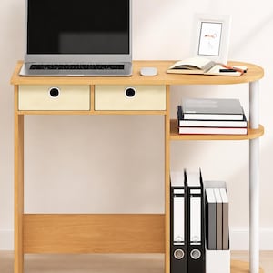 May include: A light wood-toned desk featuring two cream-colored drawers with circular pulls, a laptop, a mouse, a small picture frame, a notebook, and a pen on the surface. The side includes two open shelves holding books and document binders.