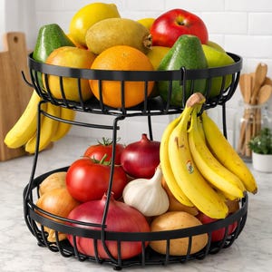 May include: A two-tiered black metal fruit basket filled with fresh produce. The top tier holds lemons, oranges, apples, avocados, and kiwis. The bottom tier contains tomatoes, red onions, garlic, potatoes, and bananas.