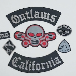 Puede incluir: Un conjunto de parches bordados que incluye un rocker negro grande con el texto Outlaws, un emblema central de calavera y pistones en gris y rojo, un rocker de California, un parche en forma de diamante 1%, un parche MC y dos parches más pequeños circulares y triangulares.