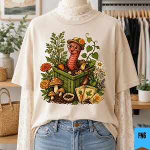 May include: A beige t-shirt featuring a graphic of a smiling worm wearing a hat and glasses inside a green wooden garden box. The design includes carrots, mushrooms, flowers, and seed packets, all rendered in a colorful, detailed illustration style.