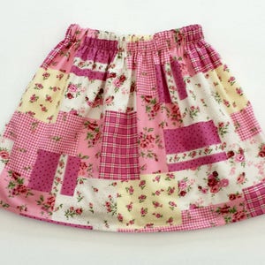 Puede incluir: Una falda de retazos rosa y amarilla con estampado floral. La falda tiene una cintura elástica fruncida.