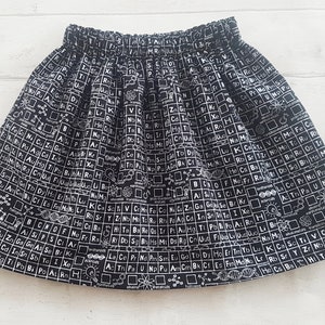 May include: A black skirt with a white print of the periodic table of elements and other science-related symbols.