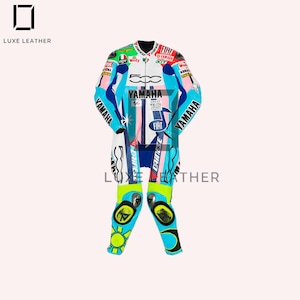 Op de afbeelding: Een wit, blauw en roze racepak met Yamaha- en Fiat-logo's. Het pak heeft een zwarte kraag en verschillende sponsorlogo's. De kniebeschermers hebben een geel zonontwerp. Het Luxe Leather-logo is zichtbaar.