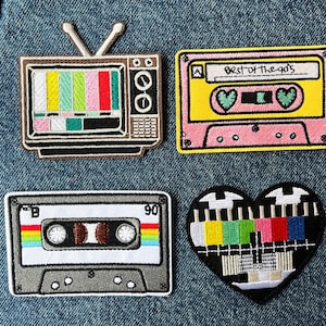 May include: Four embroidered patches featuring retro designs: a brown television with a colour test pattern, a pink and yellow cassette tape labelled Best of the 90s, a grey cassette tape with rainbow stripes, and a heart-shaped colour test pattern.