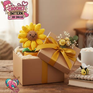 Peut inclure: Un tournesol au crochet avec un centre marron et des pétales jaunes dans un petit pot, placé dans une boîte cadeau marron avec un ruban jaune. Le couvercle est décoré de fleurs séchées. Une petite abeille au crochet est sur un livre.