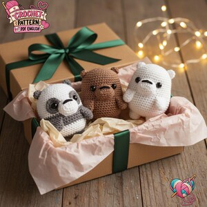 Peut inclure: Trois petites figurines d'ours au crochet de couleurs blanche, brune et grise et blanche, chacune avec des yeux en perles noires, nichées dans une boîte cadeau en carton brun nouée d'un ruban vert foncé et doublée de papier de soie beige.