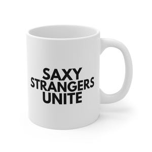 Puede incluir: Taza de cerámica blanca con el texto negro "SAXY STRANGERS UNITE". La taza tiene un asa curvada y un acabado brillante. Ideal para café, té o cualquier bebida favorita.