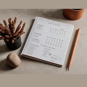 May include: An open white notebook with the text "BROW INVENTORY Daily Checklist" lies on a light surface. A pencil, a small potted plant, and a decorative stone are also present. The notebook features daily and weekly checklists.