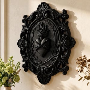 May include: Black wall art featuring a heart with flames, framed within an ornate oval and decorative border. The heart is encircled by a crown of thorns and laurel leaves. The frame has a detailed, scrollwork design.