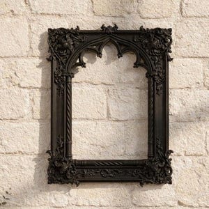 May include: Ornate black picture frame with gothic arch design. The frame features detailed carvings and a rectangular shape. The frame is mounted on a light-colored brick wall, creating a contrast between the dark frame and the neutral background.