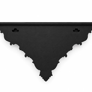 May include: A matte black wall shelf featuring a flat top surface and a decorative, triangular-shaped bracket with intricate scalloped edges. The back panel includes two pre-cut keyhole slots for mounting purposes, providing a stable structure.