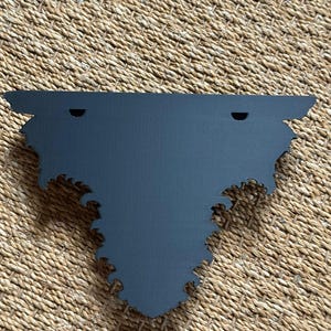 Pode incluir: Uma prateleira de parede decorativa cinza escuro com um design de borda recortada &uacute;nico e ornamentado. A prateleira tem dois orif&iacute;cios pr&eacute;-perfurados para montagem. A prateleira &eacute; feita de um material s&oacute;lido e foi projetada para ser montada na parede.