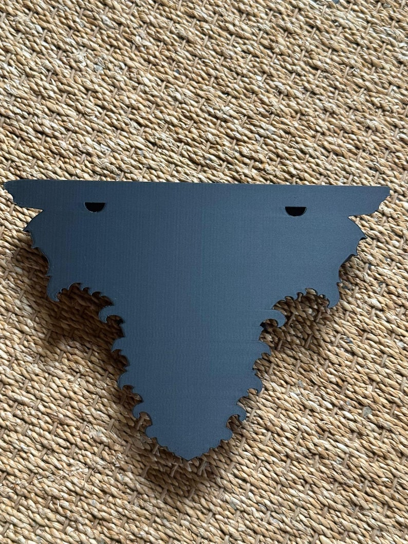 Pode incluir: Uma prateleira de parede decorativa cinza escuro com um design de borda recortada &uacute;nico e ornamentado. A prateleira tem dois orif&iacute;cios pr&eacute;-perfurados para montagem. A prateleira &eacute; feita de um material s&oacute;lido e foi projetada para ser montada na parede.