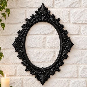 May include: An oval-shaped black picture frame featuring intricate, raised scrollwork and leaf-like carvings along the entire border. The frame has a pointed, decorative top and bottom, creating a symmetrical, elongated diamond-like silhouette.