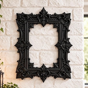 May include: A rectangular black picture frame featuring intricate, ornate, and symmetrical carved scrollwork and leaf-like patterns along its entire border, with a central open space for displaying a photograph or artwork.