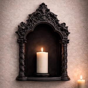 May include: A black, ornate wall-mounted candle holder with a lit white pillar candle inside. The holder has a decorative arched top and twisted column-like sides. Another lit candle sits to the right, creating a warm, inviting ambiance.