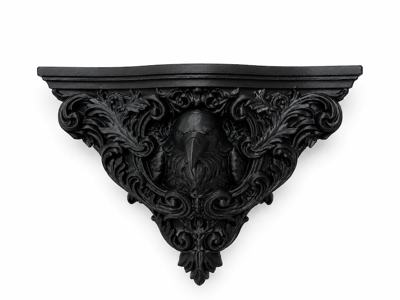 May include: A matte black wall shelf featuring a central sculpted raven head surrounded by intricate, symmetrical acanthus leaf scrollwork. The shelf has a flat top surface and a decorative, pointed bracket base with detailed relief carvings.