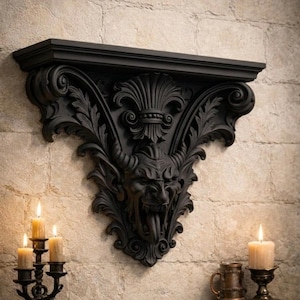 Pode incluir: Prateleira de parede preta e ornamentada com um design de rosto de dem&ocirc;nio. A prateleira &eacute; montada em uma parede de tijolos texturizada e de cor clara. Um casti&ccedil;al preto com velas acesas est&aacute; &agrave; esquerda. Uma vela e uma caneca est&atilde;o &agrave; direita.