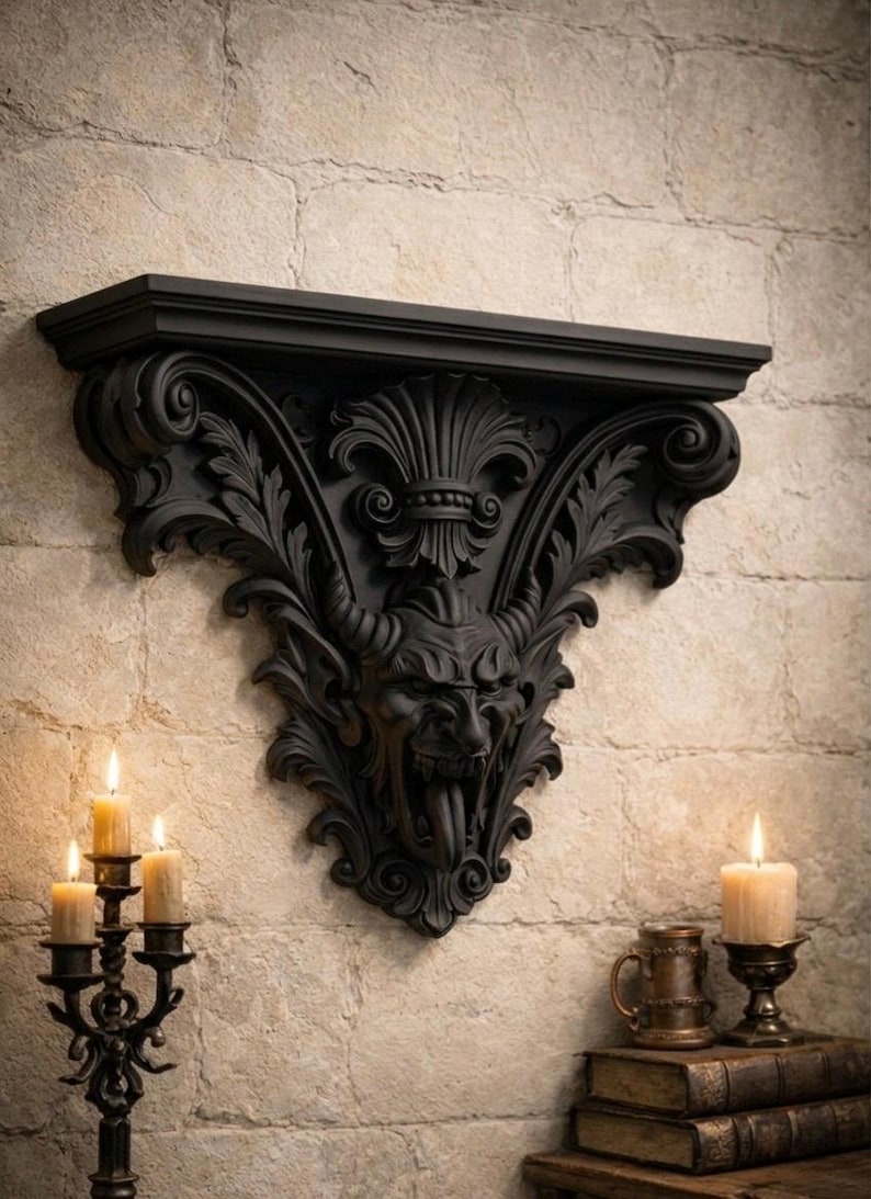 Pode incluir: Prateleira de parede preta e ornamentada com um design de rosto de dem&ocirc;nio. A prateleira &eacute; montada em uma parede de tijolos texturizada e de cor clara. Um casti&ccedil;al preto com velas acesas est&aacute; &agrave; esquerda. Uma vela e uma caneca est&atilde;o &agrave; direita.