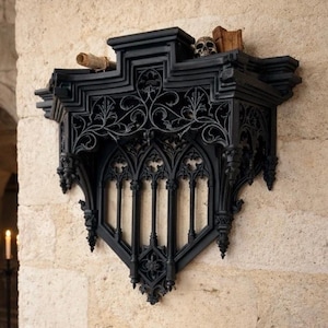 May include: A black gothic-style wall shelf with intricate scrollwork and pointed arches. The shelf is mounted on a textured stone wall. A small skull, a rolled scroll, and a book rest on the shelf.