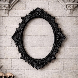 May include: An oval-shaped picture frame in a matte black finish, featuring intricate relief carvings of floral and leaf motifs along the border. The frame has a symmetrical design with prominent decorative elements at the top and bottom.