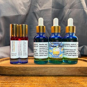 Puede incluir: Una bandeja de madera contiene dos peque&ntilde;os frascos roll-on y tres botellas de vidrio azul con tapas doradas. Las botellas contienen aceite para cut&iacute;culas, con etiquetas que incluyen texto.