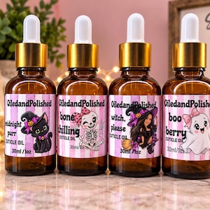 May include: Four amber glass dropper bottles of cuticle oil, each with a gold cap and a label featuring pink stripes and Halloween-themed illustrations. The labels read OiledandPolished, with names Midnight Purr, Bone Chilling, Witch Please, and Boo Berry.