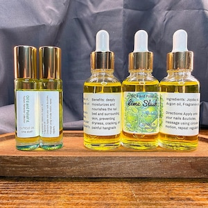 Puede incluir: Una bandeja de madera contiene cuatro botellas de aceite para cut&iacute;culas y dos botellas con rodillo. Las botellas tienen tapas y cuentagotas dorados, llenos de un l&iacute;quido amarillo. Las etiquetas dicen "Lime Slush" y "Cuticle Oil".