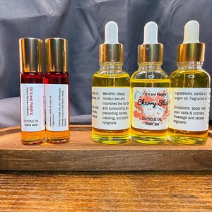 Puede incluir: Una bandeja de madera contiene dos botellas roll-on y tres botellas con cuentagotas de aceite para cut&iacute;culas. Las botellas roll-on est&aacute;n etiquetadas como "Oil'd and Polish'd" y "cherry slush". Las botellas con cuentagotas est&aacute;n etiquetadas como "Cherry Slush" y "CUTICLE OIL 30ml/1oz."