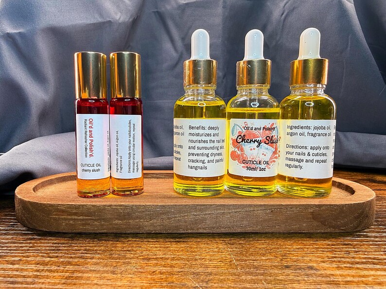 Puede incluir: Una bandeja de madera contiene dos botellas roll-on y tres botellas con cuentagotas de aceite para cut&iacute;culas. Las botellas roll-on est&aacute;n etiquetadas como "Oil'd and Polish'd" y "cherry slush". Las botellas con cuentagotas est&aacute;n etiquetadas como "Cherry Slush" y "CUTICLE OIL 30ml/1oz."