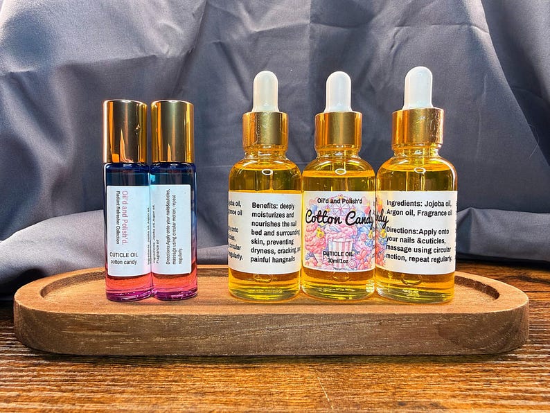 Puede incluir: Una bandeja de madera contiene varias botellas peque&ntilde;as de vidrio con aceite para cut&iacute;culas. Las botellas tienen tapas y cuentagotas dorados. Las etiquetas dicen "Cotton Candy" y "Cuticle Oil". Los aceites son para hidratar y nutrir las u&ntilde;as y cut&iacute;culas.