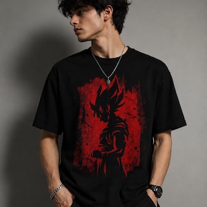 May include: A black short-sleeved t-shirt featuring a graphic print of a spiky-haired anime character silhouette in black against a distressed, textured red rectangular background. The design is centered on the chest of the garment.