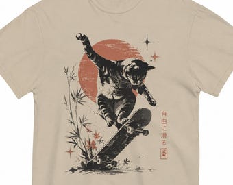 May include: A beige t-shirt featuring a graphic of a tabby cat performing a trick on a skateboard. The design includes a large red sun, bamboo stalks, and four-pointed stars. Japanese text reads 自由に滑る next to a small red square with a paw print.