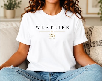 May include: A white short-sleeve t-shirt featuring the black text WESTLIFE centered on the chest. Below the text is a thin gold horizontal line with a small star in the center, followed by the gold text 25 YEARS printed underneath.