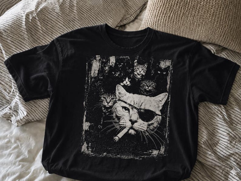 May include: Black t-shirt featuring a distressed graphic of a cat wearing an eye patch and sunglasses, smoking a cigarette, surrounded by other cats. The design is in shades of white and gray.